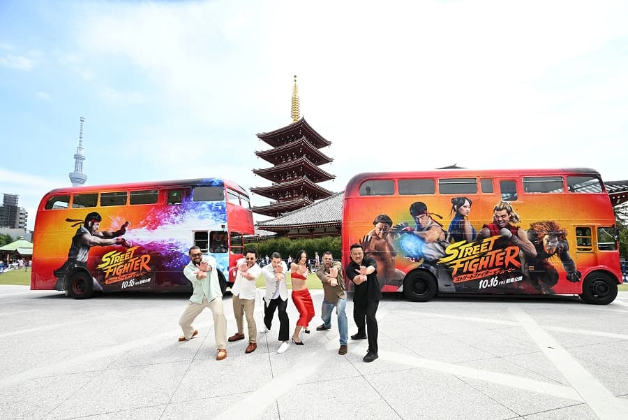 Cast and director posing between two Street Fighter wrapped buses in front of Senso-ji's pagoda